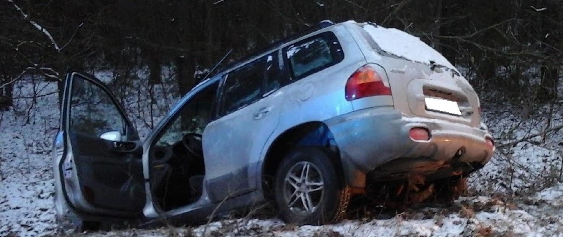 Samochód osobowy stojący przodem w przydrożnym rowie. Teren wokół pokryty śniegiem. Widok z drogi.