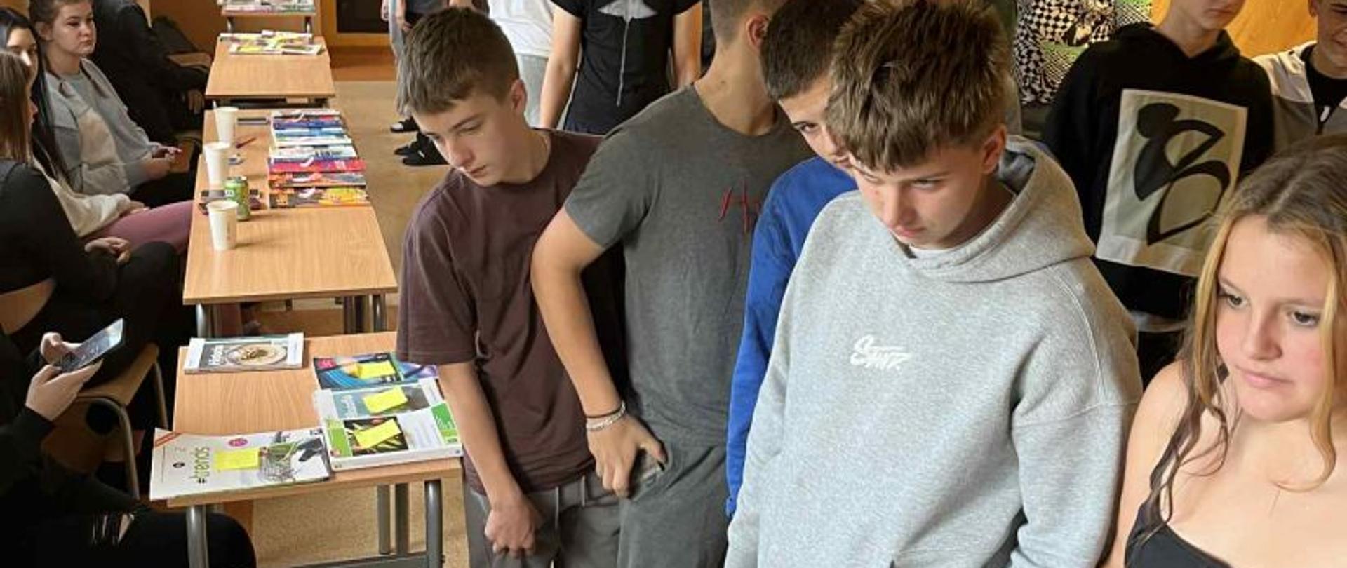 Wielu uczniów zgromadzonych przy stolikach, na których wyłożono podręczniki