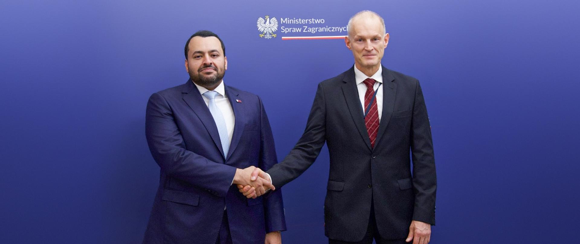Undersecretary of State at the Ministry of Foreign Affairs Wojciech Zajączkowski is shaking hands with the Minister of State at the Ministry of Foreign Affairs of the State of Qatar Mohammed bin Abdulaziz Al-Khulaifi in Warsaw. They stand on a navy blue background with the Polish MFA logo. 