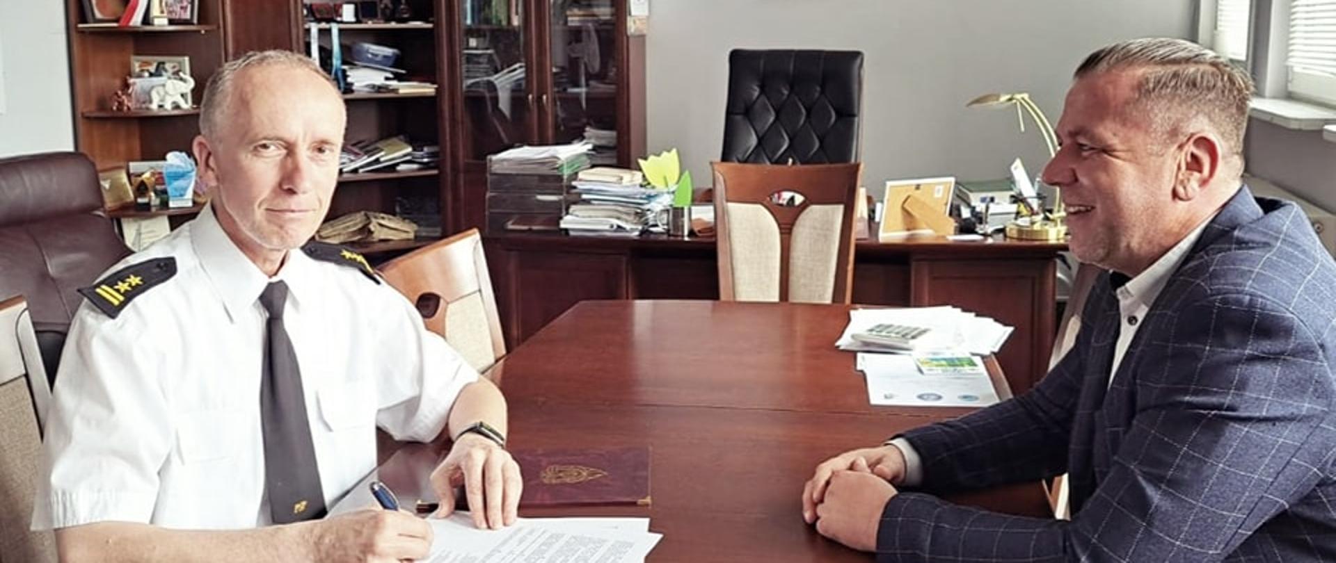 Zdjęcie przedstawia podpisanie umowy wsparcia na zakup ciężkiego samochodu ratowniczo gaśniczego. Przy biurku siędzi burmistrz oraz komendant powiatowy psp podpisujący umowę.
