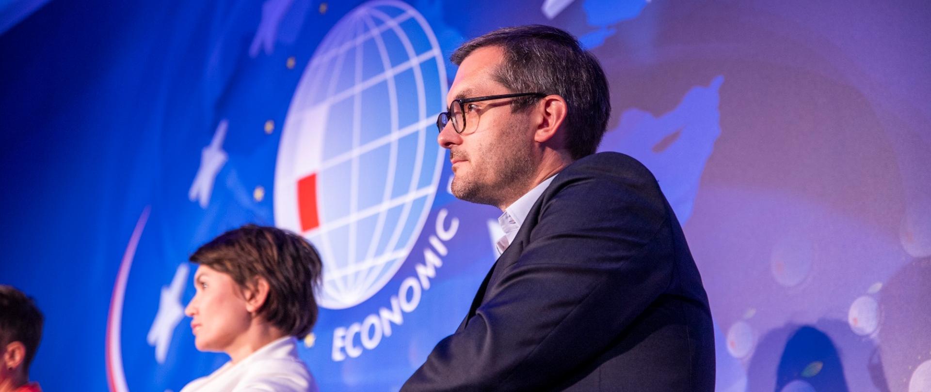 Wiceminister na tle niebieskiej ściany z logiem Forum