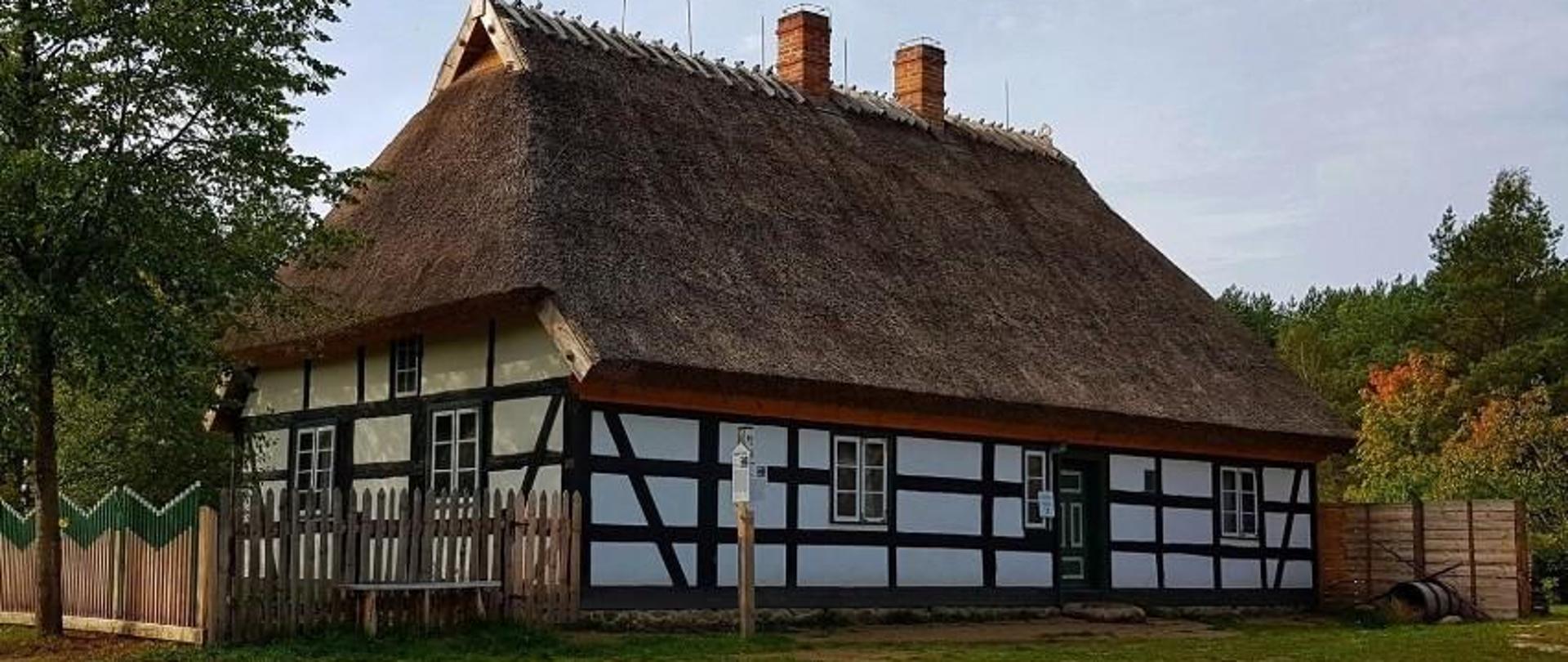 Chałupa z Garcza, z murem pruskim, wokół niej płot, drzewa i trawa