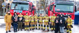 Zdjęcie przedstawia strażaków Komendy Powiatowej Państwowej Straży Pożarnej w Gołdapi, którzy wspólnie z wolontariuszami Wielkiej Orkiestry Świątecznej Pomocy uczestniczą w 32. Finale na Placu Zwycięstwa w Gołdapi. W tle widać dwa pojazdy pożarnicze. Niektóre osoby ujęte na obrazie, posiadają na swojej odzieży naklejone serce Wielkiej Orkiestry Świątecznej Pomocy