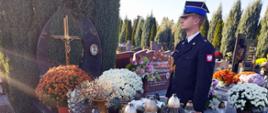 Widok z przodu. Strażak stoi obok grobu. Na drugim planie inne mogiły.