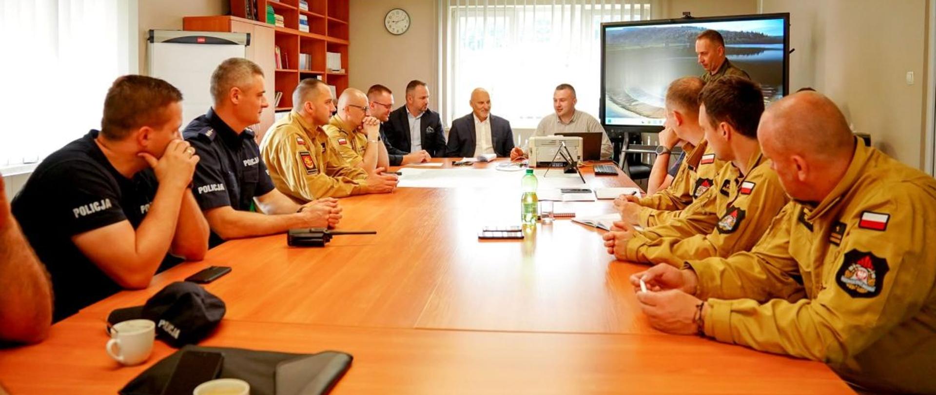 Zdjęcie przedstawia przedstawicieli służb oraz władz powiatu siedzących przy stole w sztabie. 