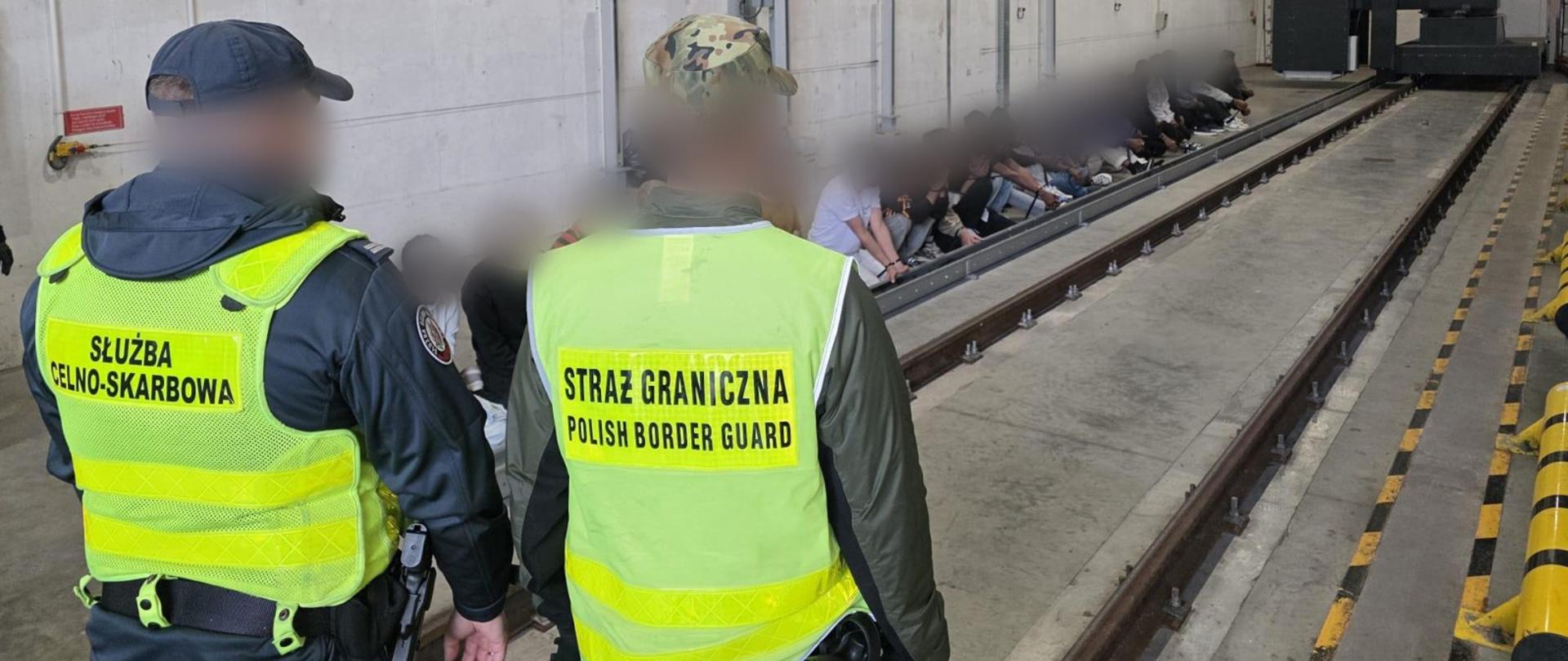 Funkcjonariusze podlaskiej Służby Celno-Skarbowej i podlaskiej Straży Granicznej. Przed nimi zatrzymani nielegalni migranci.