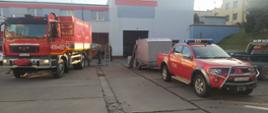 Sprzęt pożarniczy dla ukraińskich strażaków. Komenda Powiatowa PSP w Gostyniu. Strażacy przygotowują do transportu zebrany sprzęt. Na placu komendy stoi samochód ciężarowy, na który za pomocą wózka widłowego ładowana jest europaleta ze sprzętem. Obok samochodu znajduje się 2 strażaków. Z prawej strony zaparkowany jest samochód rozpoznawczo ratowniczy, do którego podczepiona jest przyczepka. W tle budynek garażowy. 