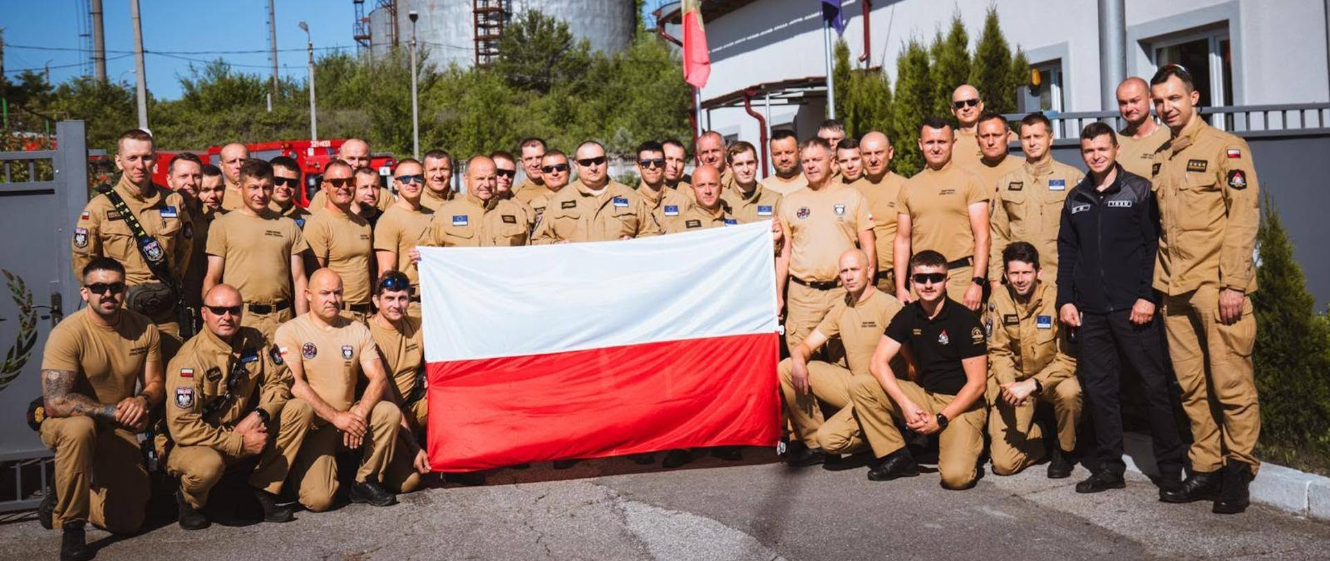 Grupa strażaków Państwowej Straży Pożarnej uczestniczących w ćwiczeniach EU MODEX Mołdawia 2026 pozuje do zdjęcia z flagą Polski.
