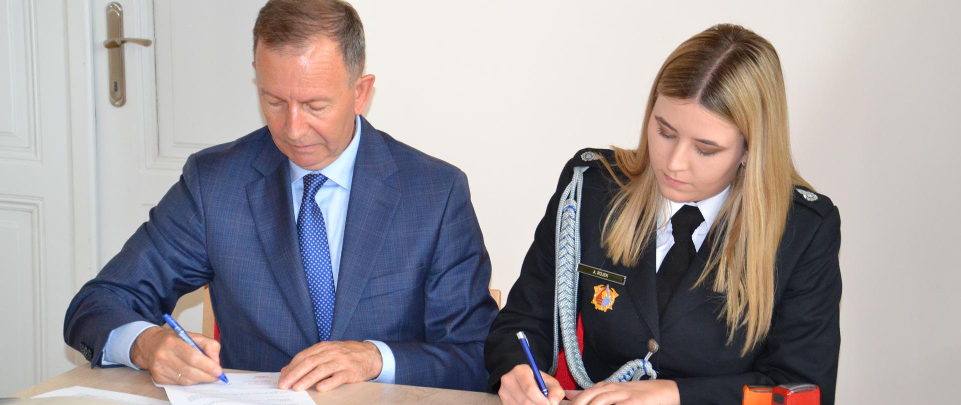 Zdjęcie przedstawia moment podpisywania umowy na dofinansowanie sprzętu przy stole prezydialnym przez Prezesa OSP Ropczyce-Chechły Annę Rojek oraz Zastępcy Prezesa WFOŚiGW w Rzeszowie Bogusława Kidę