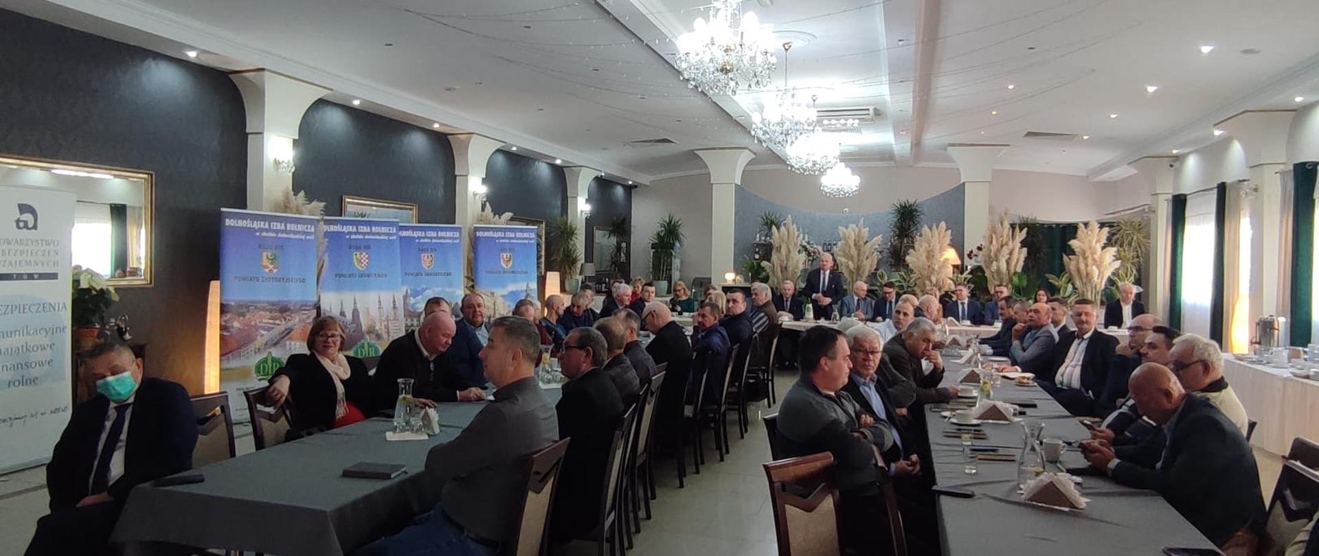 Uczestnicy Forum siedzący przy stołach ustawionych w kształt litery "U". Po boku banery Dolnośląskiej Izby Rolniczej.