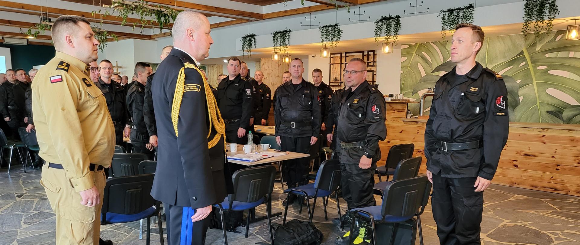 strażak składa meldunek drugiemu strażakowi, w tle grupa strażaków stojąca na baczność 