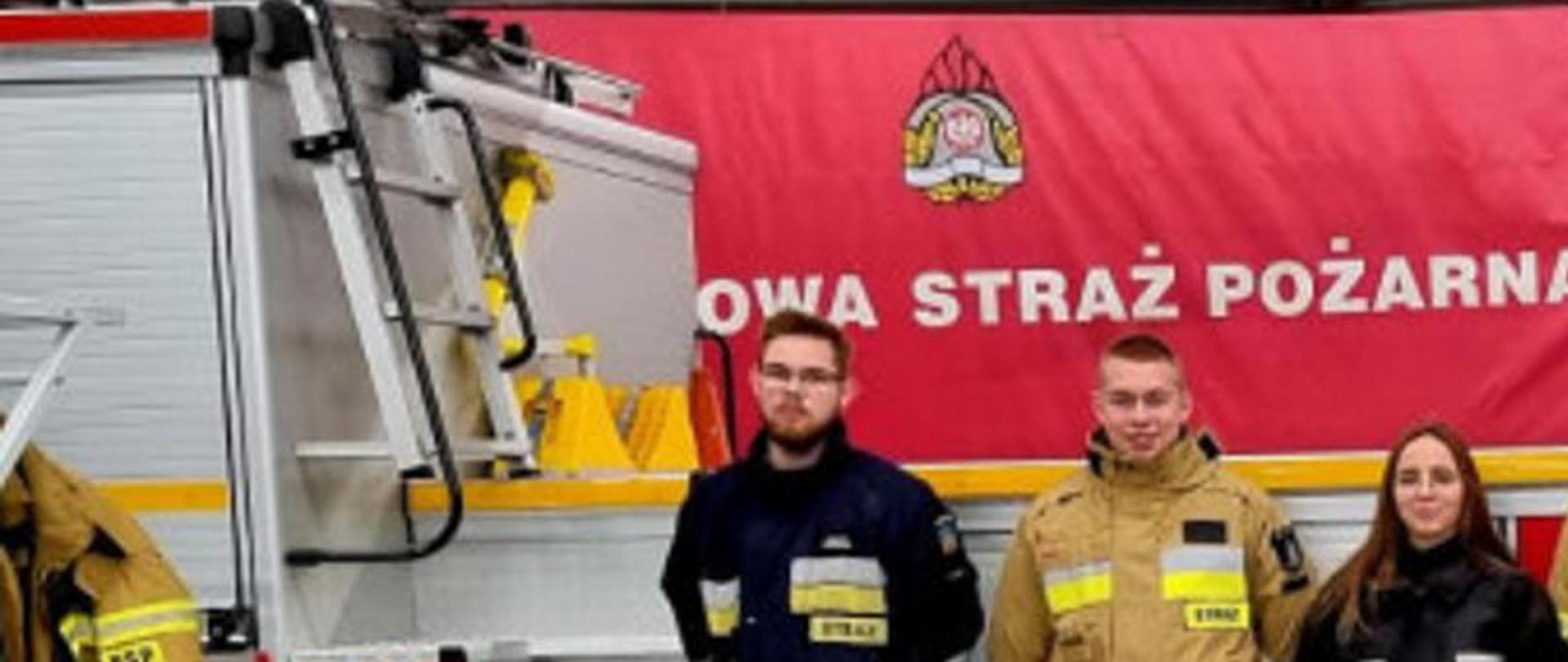 Zdjęcie przedstawia ośmiu strażaków stojących przy wozie pożarniczym