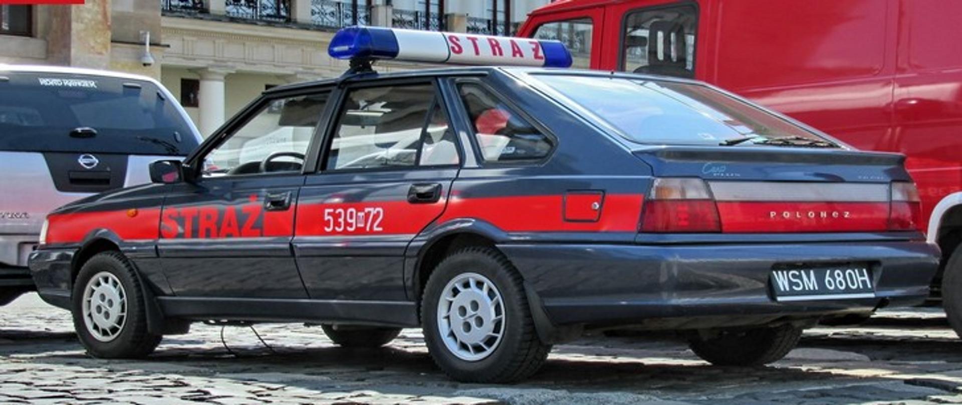 Zdjęcie przedstawia strażacki samochód osobowy Polonez, w kolorze grafitowym, z czerwonym napisem STRAŻ.