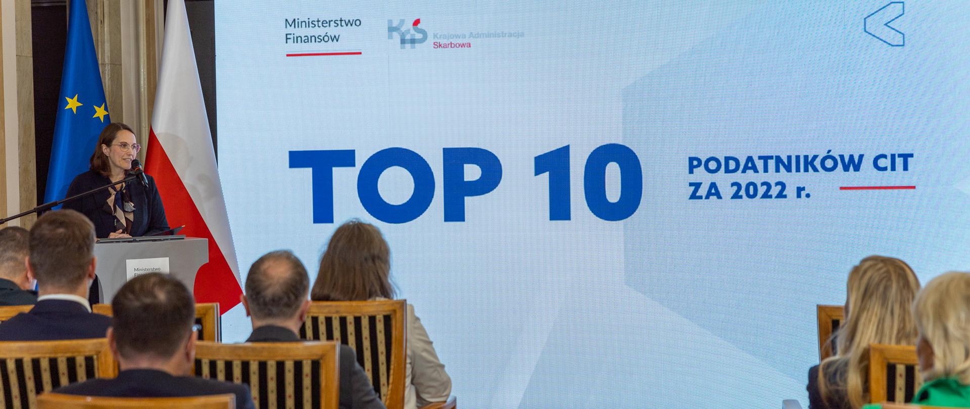 Minister finansów Magdalena Rzeczkowska na tle napisu TOP 10 podatników CIT za 2022 r.