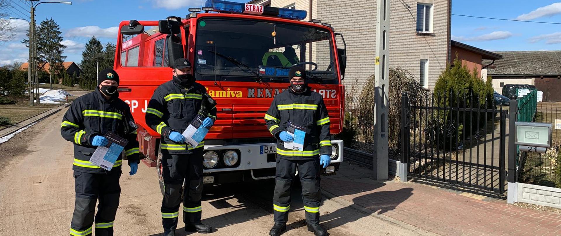 Na zdjęciu widoczni strażacy oraz samochód pożarniczy podczas akcji kolportażu ulotek na terenie gm. Sztabin. 