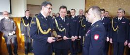 Komendant i zastępca komendanta powiatowego wręczają strażakowi pamiątkowy prezent.