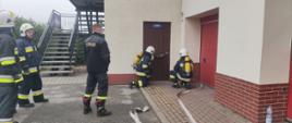 Zdjęcie przedstawia plac Komendy Powiatowej Państwowej Straży Pożarnej w Radziejowie oraz strażaków OSP podczas wykonywania ćwiczenia wejścia do strefy zagrożonej z linią wężową.