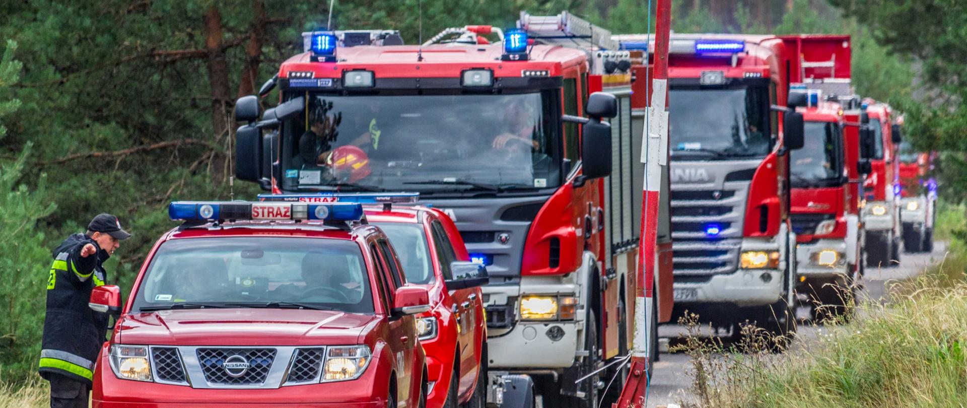 Strażak wskazuje przybyłym samochodom pożarniczym miejsce stacjonowania.