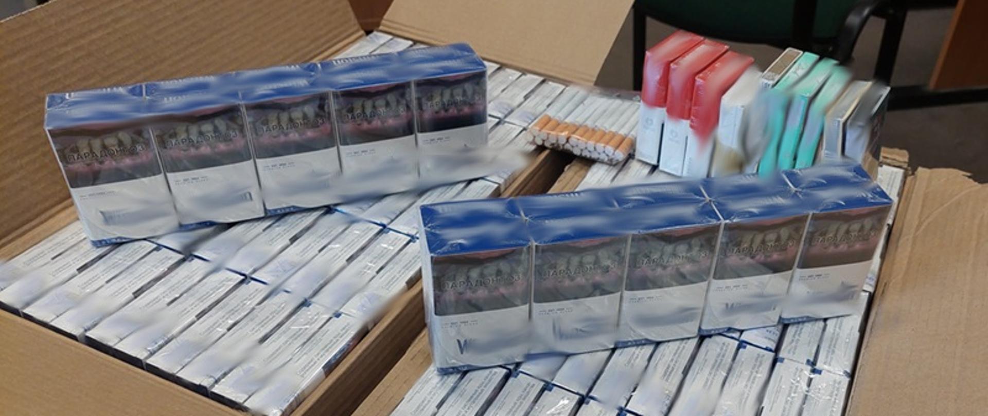 Paczki z papierosami ułożone w dwóch kartonach. Część papierosów ułożona i postawiona na wierzchu. 