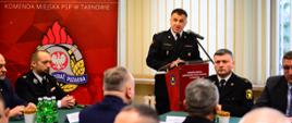 Na zdjęciu widzimy przemawiającego Komendanta Miejskiego PSP w Tarnowie . Komendant
ma oparte ręce na mównicy stoi na tle banneru KM PSP w Tarnowie oraz na tle okna. Obok niego po prawej stronie widoczni są mężczyźni siedzący za stołem na którym widoczny jest zielony obrus, woda mineralna i paluszki. Na zdjęciu widoczni są również mężczyźni siedzący przodem do siebie.
Komendant występuje w umundurowaniu galowym.
Na pierwszym planie widoczni są uczestnicy narady którzy siedzą przy dwóch stołach nakrytych zielonym obrusem.
