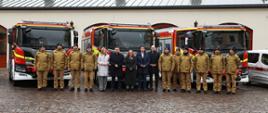 Zdjęcie grupowe uczestników uroczystości na tle samochodów pożarniczych