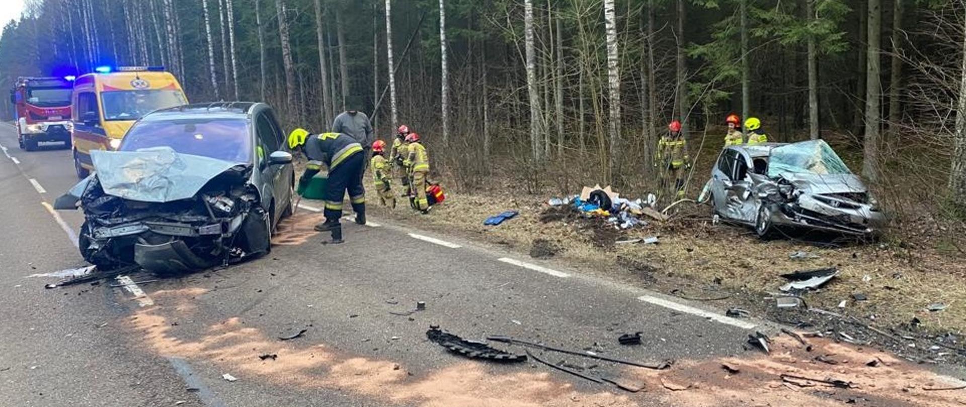 Dwa rozbite samochody osobowe. Jeden stoi na drodze, 2 znajduje się na poboczu. Za nimi stoi ZRM oraz PSP. 
