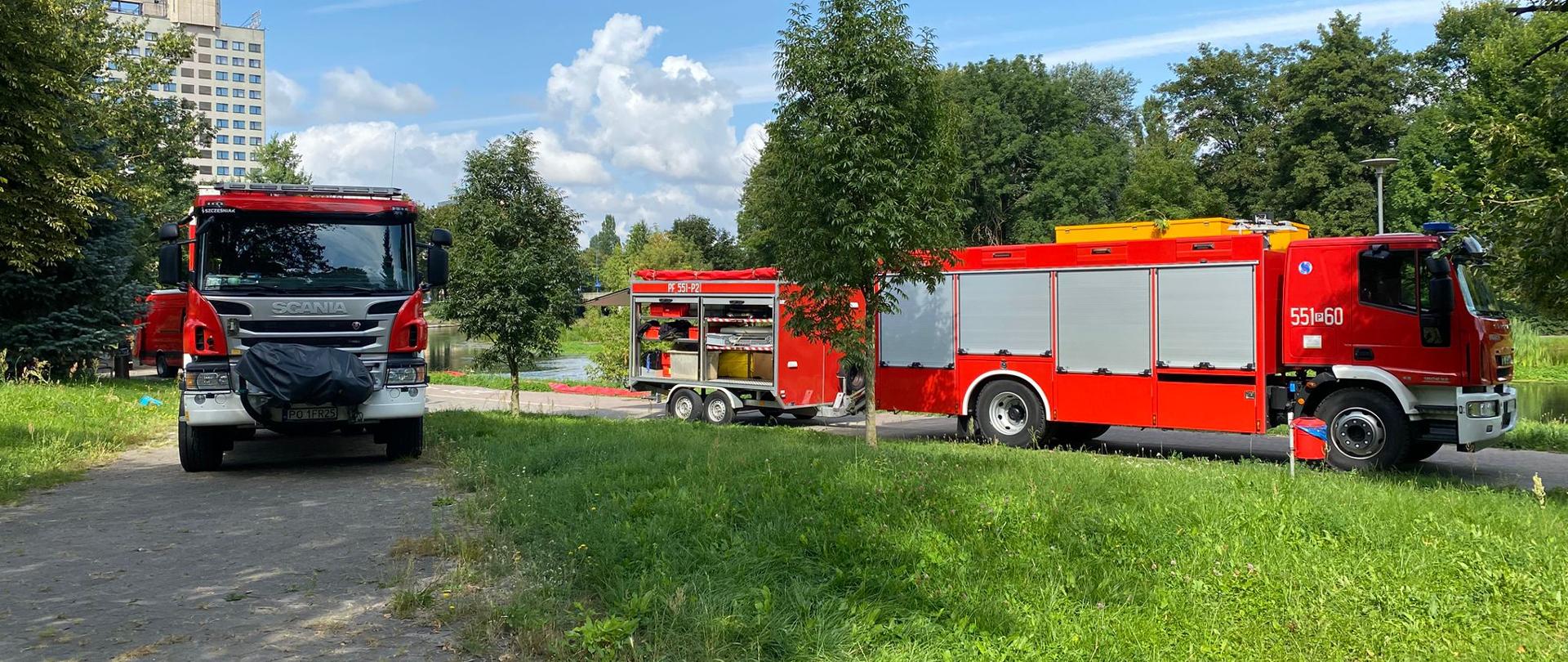 Na zdjęciu widnieją strażacy oraz pojazdy ratownicze w trakcie ćwiczeń nad rzeką. 