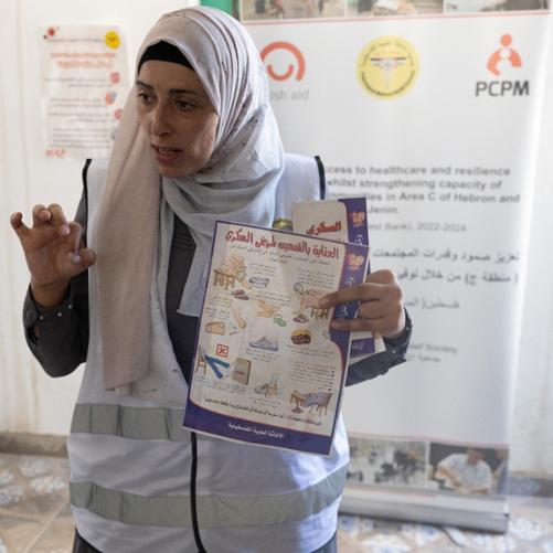 Kobieta z ulotką dotyczącą cukrzycy w alfabecie arabskim z rysunkami, w tle banner z logo Polska pomoc