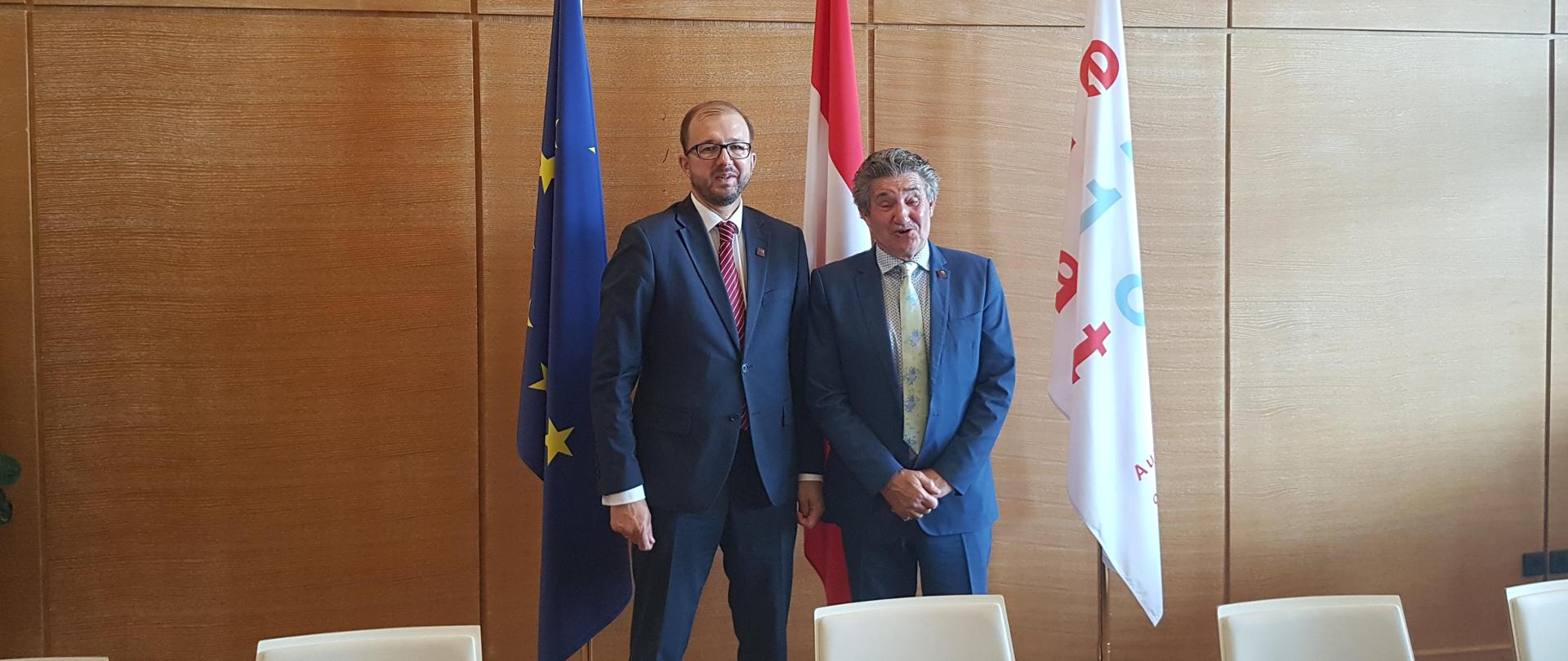 Minister Dardziński na tle ściany i flag Polski i UE