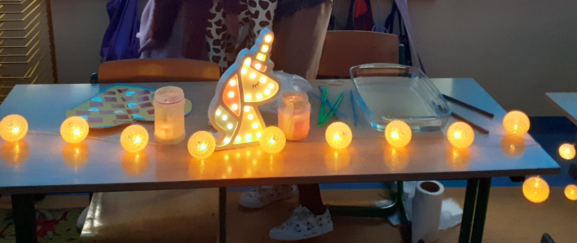 Zdjęcie dzieci w półmroku. Poniżej stół z lampkami.