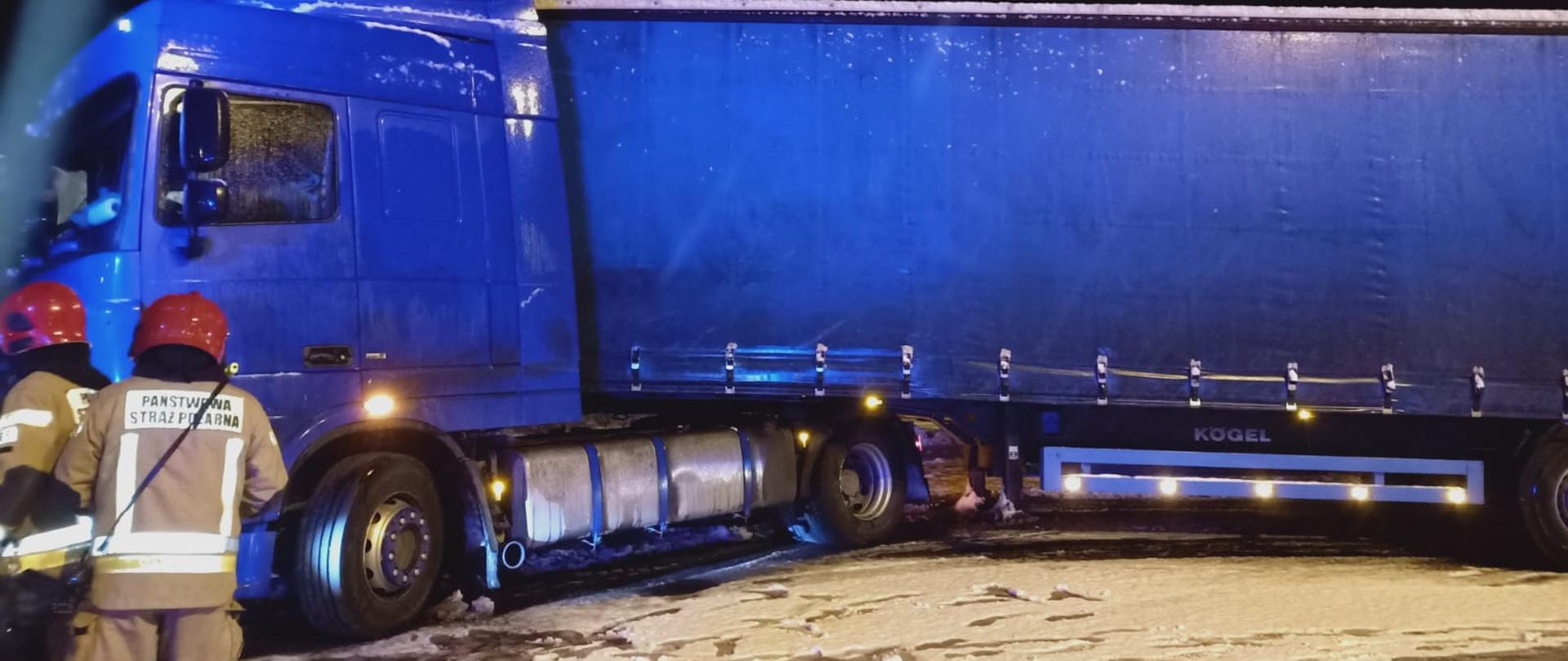 Na zdjęciu widać samochód ciężarowy na rondzie oraz dwóch strażaków 