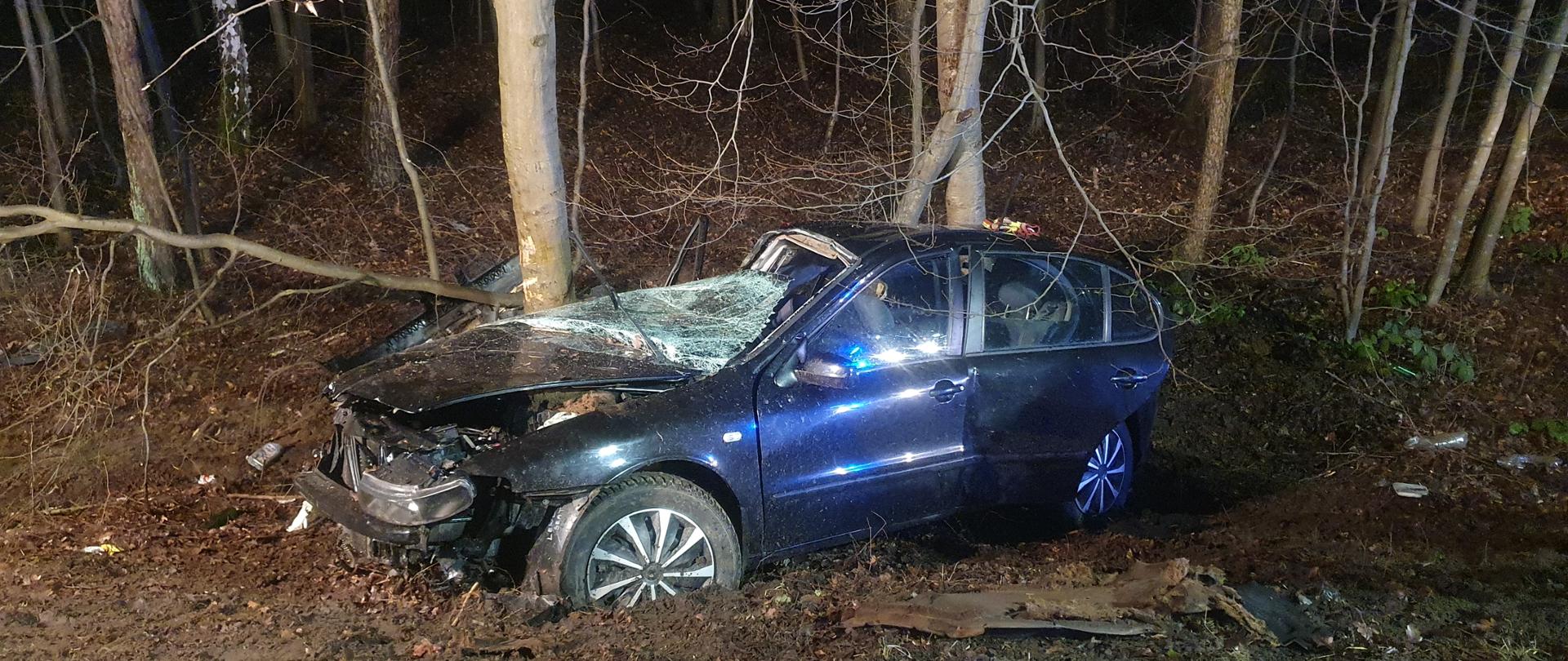 Zdjęcie przedstawia zniszczony samochód stojący na kołach w przydrożnym rowie.