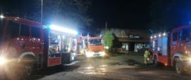 Na zdjęciu widać samochody pożarnicze biorące udział w akcji, które oświetlają teren działań. Jest noc w tle widać budynek gastronomiczny w którym doszło do pożaru