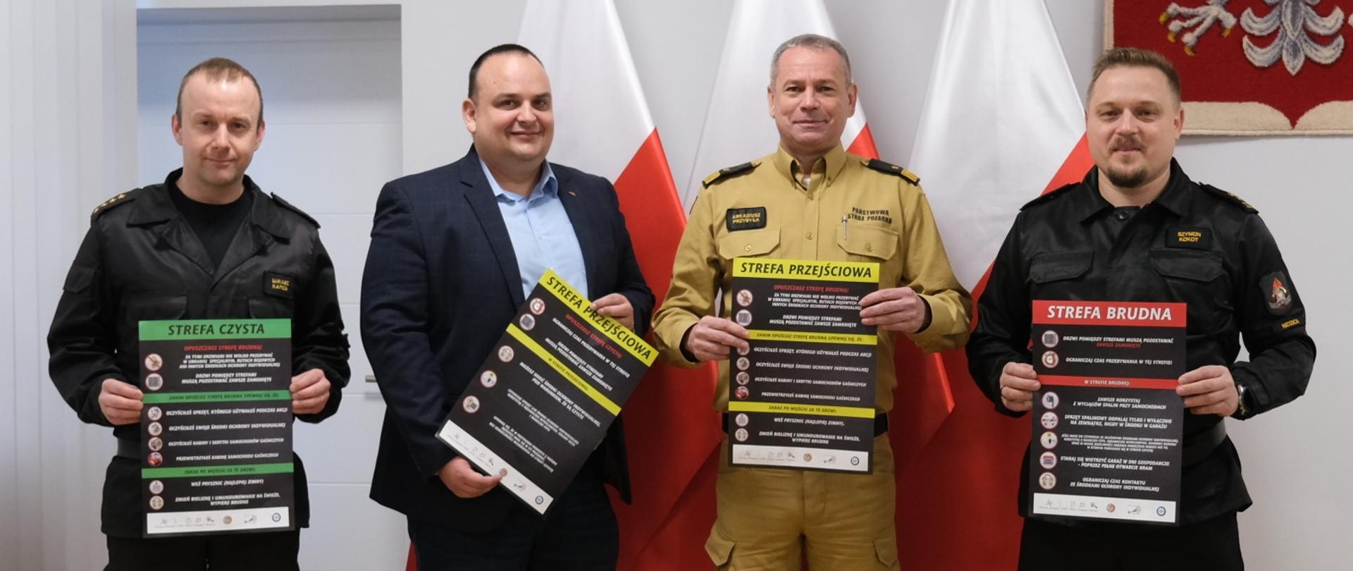 Na zdjęciu widać czterech strażaków trzymających plakaty z napisami w kolorze białym na czarnym tle.