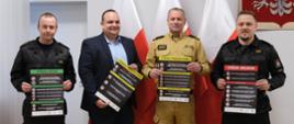 Na zdjęciu widać czterech strażaków trzymających plakaty z napisami w kolorze białym na czarnym tle.