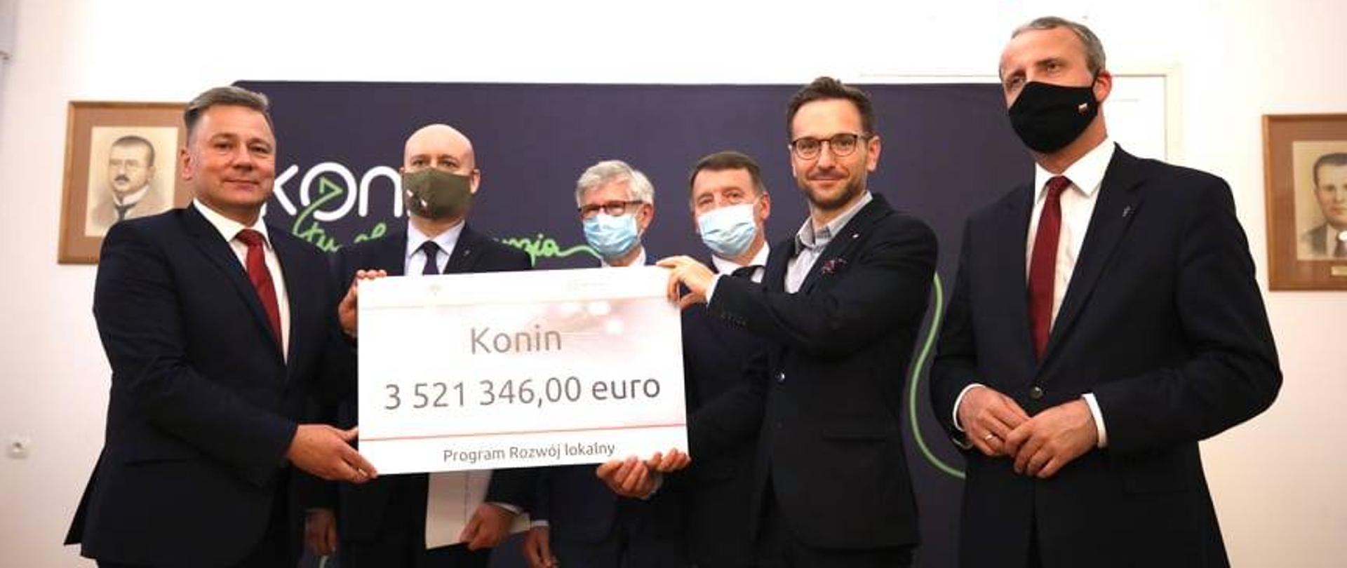 Na zdjęciu minister Waldemar Buda wręcza czek prezydentowi miasta Konin Piotrowi Korytkowskiemu. Na czeku widnieje napis Konin, kwota 3521346,00 euro w ramach Programu Rozwój Lokalny. Na zdjęciu grupowym znajduje się również lokalni parlamentarzyści oraz wojewoda wielkopolski. 