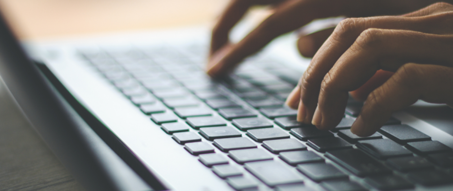 Ręce piszące na klawiaturze laptopa, z rozmytym tłem i wyraźnym zbliżeniem na palce naciskające klawisze.