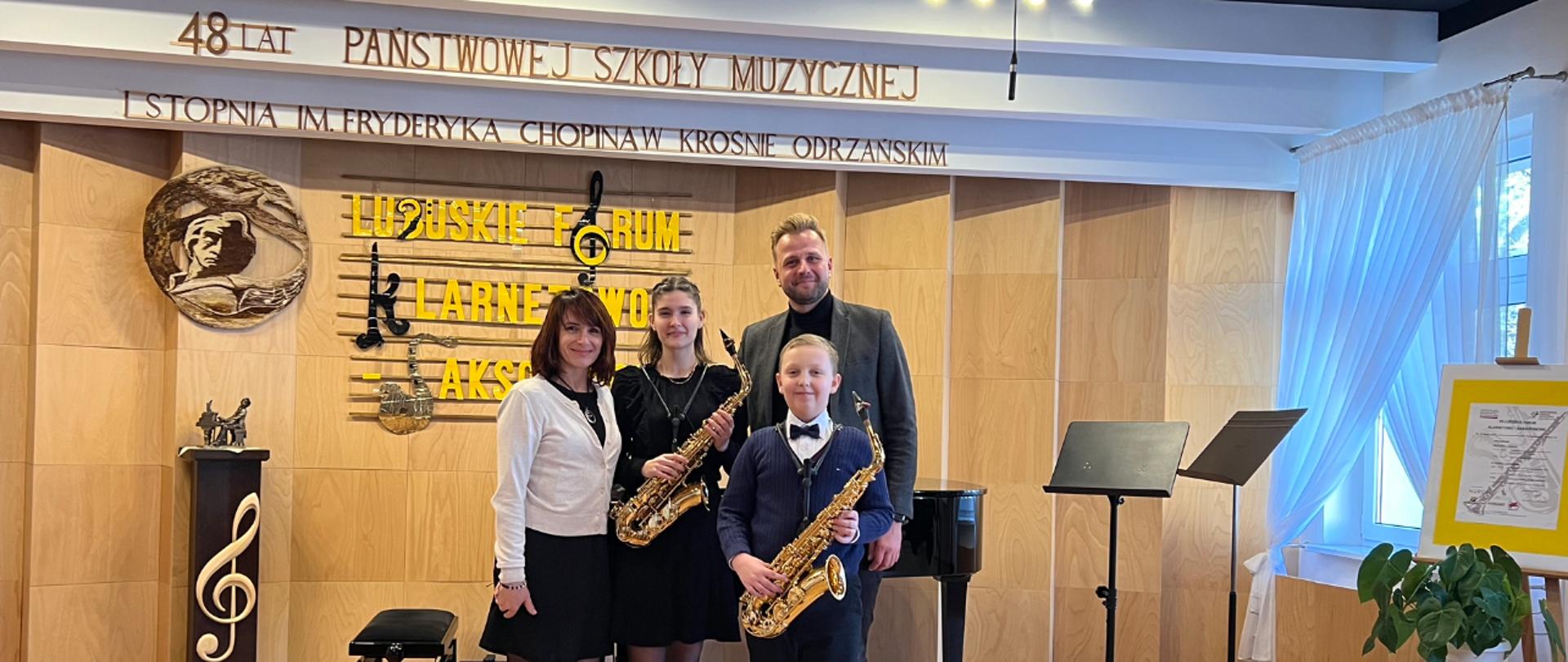 Zdjęcie grupowe przedstawiające od lewej strony Panią Halynę Hachak oraz Oliwię Mikołajewską i Ruslana Krutii z saksofonem, a także Pana Mateusza Boducha podczas VII Lubuskiego Forum Klarnetowo-Saksofonowego.