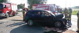 Rozbita osobowa honda stoi na skrzyżowaniu, strażacy obsypują sorbentem miejsce wypadku