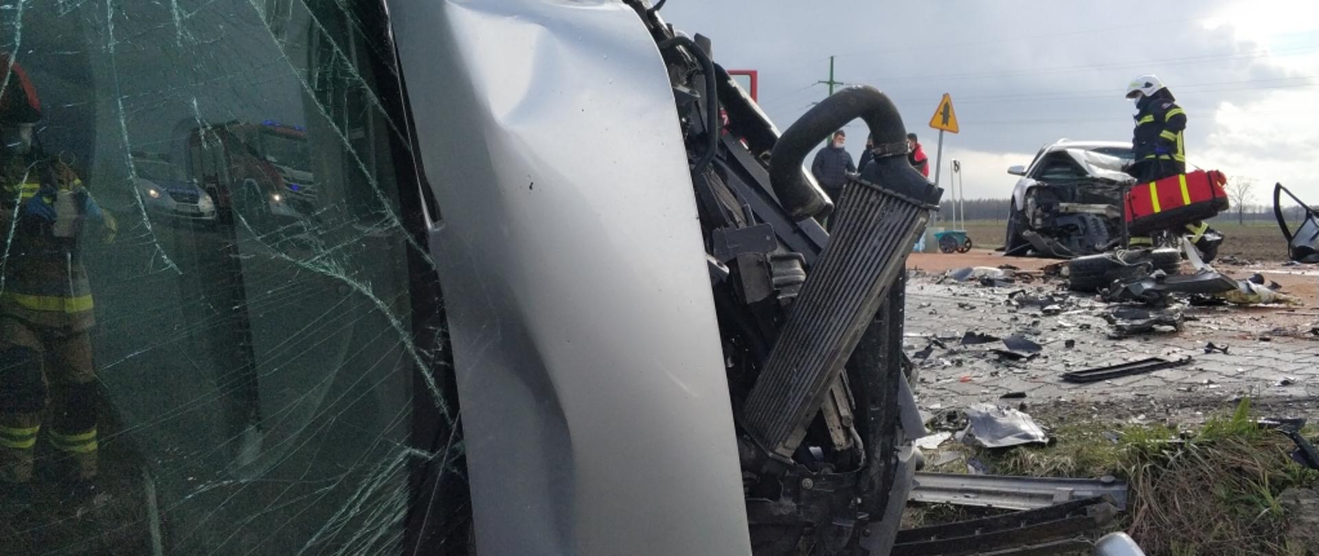 Samochody osobowe po wypadku oraz strażak przechodzący z torbą medyczną.