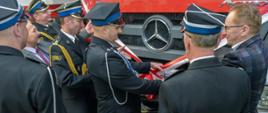Druhowie OSP przecinający wstęgę przy odbiorze samochodu ratowniczo-gaśniczego dla jednostki OSP KSRG Glinojeck