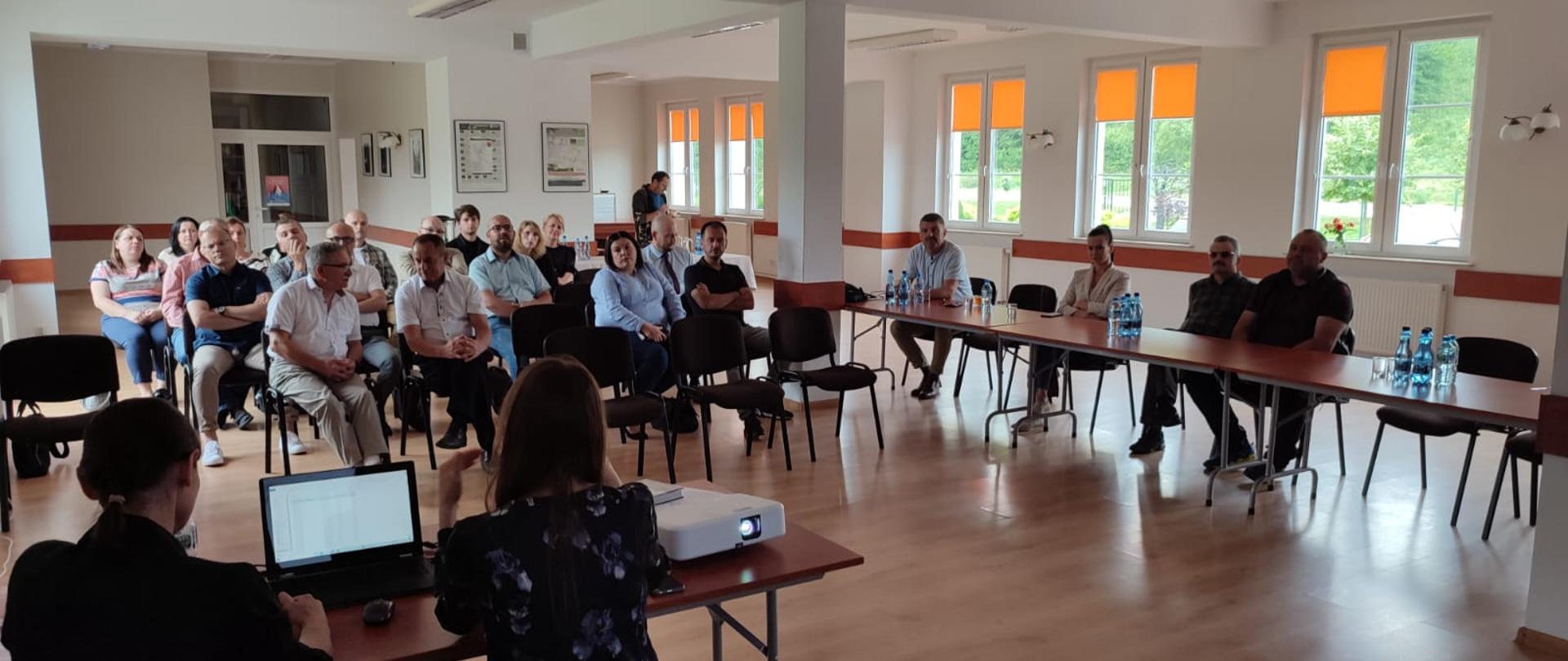 grupa ludzi na sali wykładowej, na pierwszym planie po lewej prowadzące spotkanie, tyłem do kadru