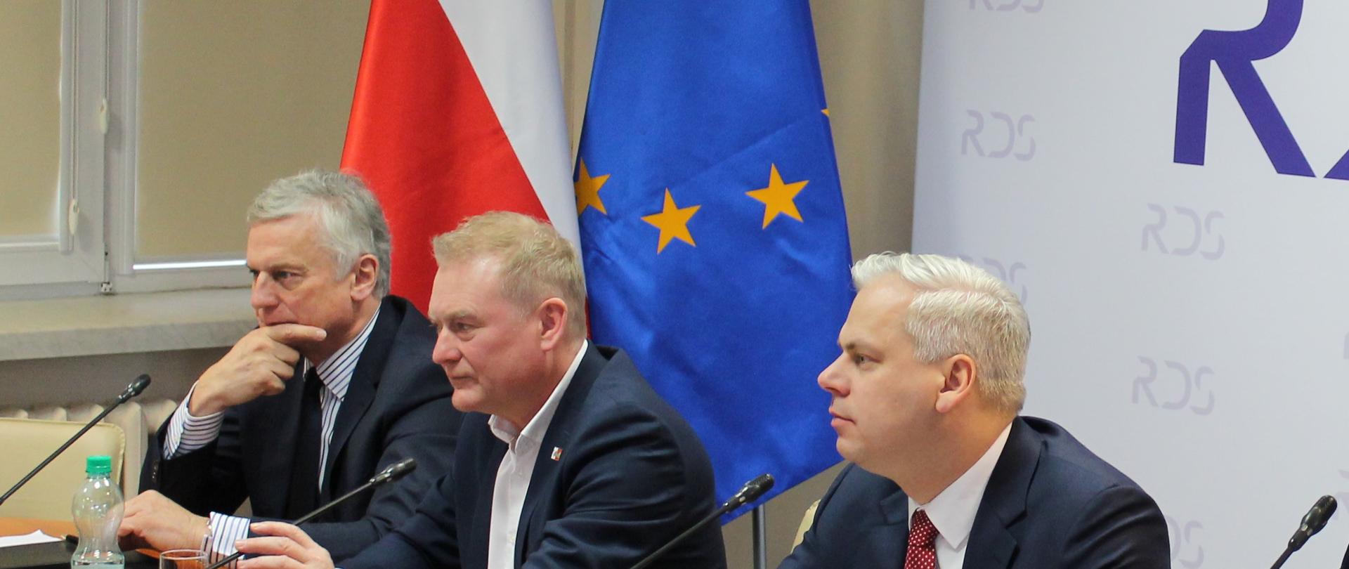 Zdjęcie przedstawia Współprzewodniczących Zespołu siedzących za stołem prezydialnym – Karola Rabendę - Podsekretarza Stanu w Ministerstwie Aktywów Państwowych, Współprzewodniczącego ze strony rządowej, Krzysztofa Kisielewskiego – Współprzewodniczącego ze strony związków zawodowych oraz Ryszarda Wasiłka – Współprzewodniczącego ze strony pracodawców. W tle znajdują się dwie flagi – Polski i UE oraz baner Rady Dialogu Społecznego.