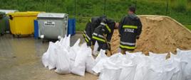 Strażacy ratownicy napełniają worki z piachem.