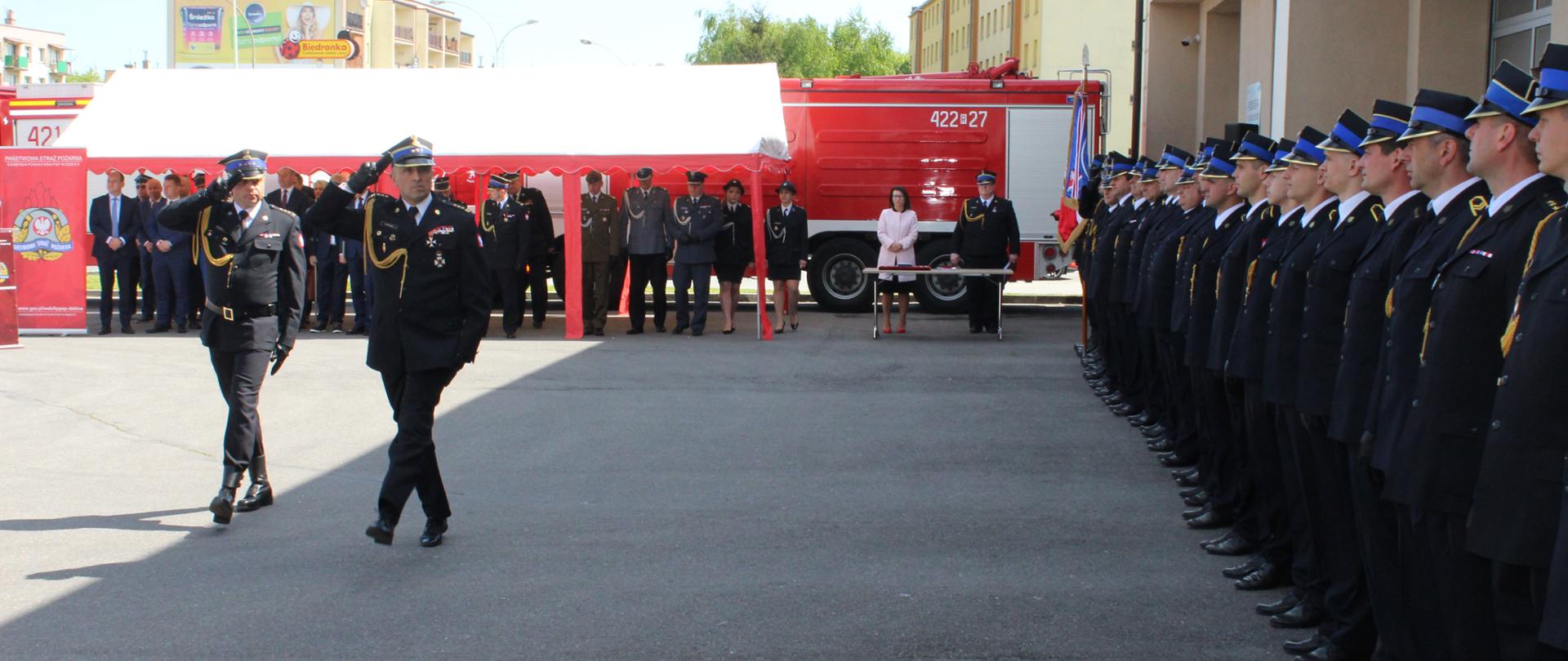 Na zdjęciu zastępca podkarpackiego komendanta wojewódzkiego Państwowej Straży Pożarnej, w asyście dowódcy uroczystości, dokonuje przeglądu pododdziałów. Strażacy ubrani są w mundury galowe i stoją na placu zewnętrznym przy budynku komendy. Goście znajdują się pod namiotem ustawionym na tą okoliczność.
