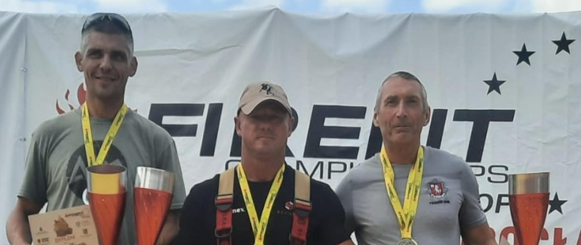 Zdjęcie przedstawia trzech strażaków na podium, jeden z flagą Polski.