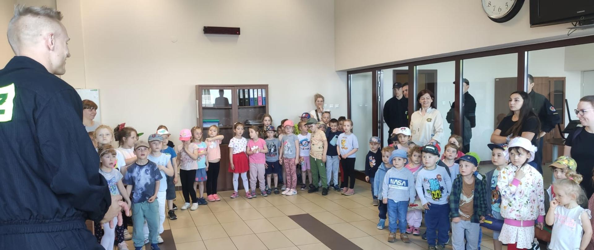Po lewej strażak, wokół niego zgromadzona grupa przedszkolaków wraz z Paniami opiekunkami