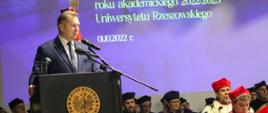 Minister Czarnek stoi przy mównicy i mówi do mikrofonu, za nim ściana z napisem Inauguracja roku akademickiego.
