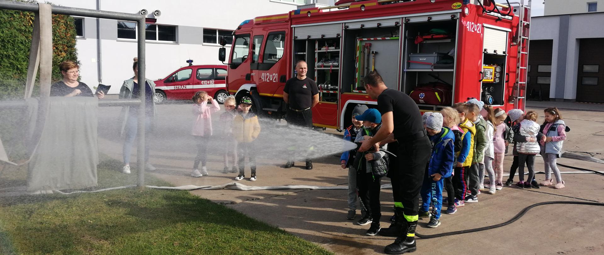 Dzieci leją wodę z węża strażackiego.