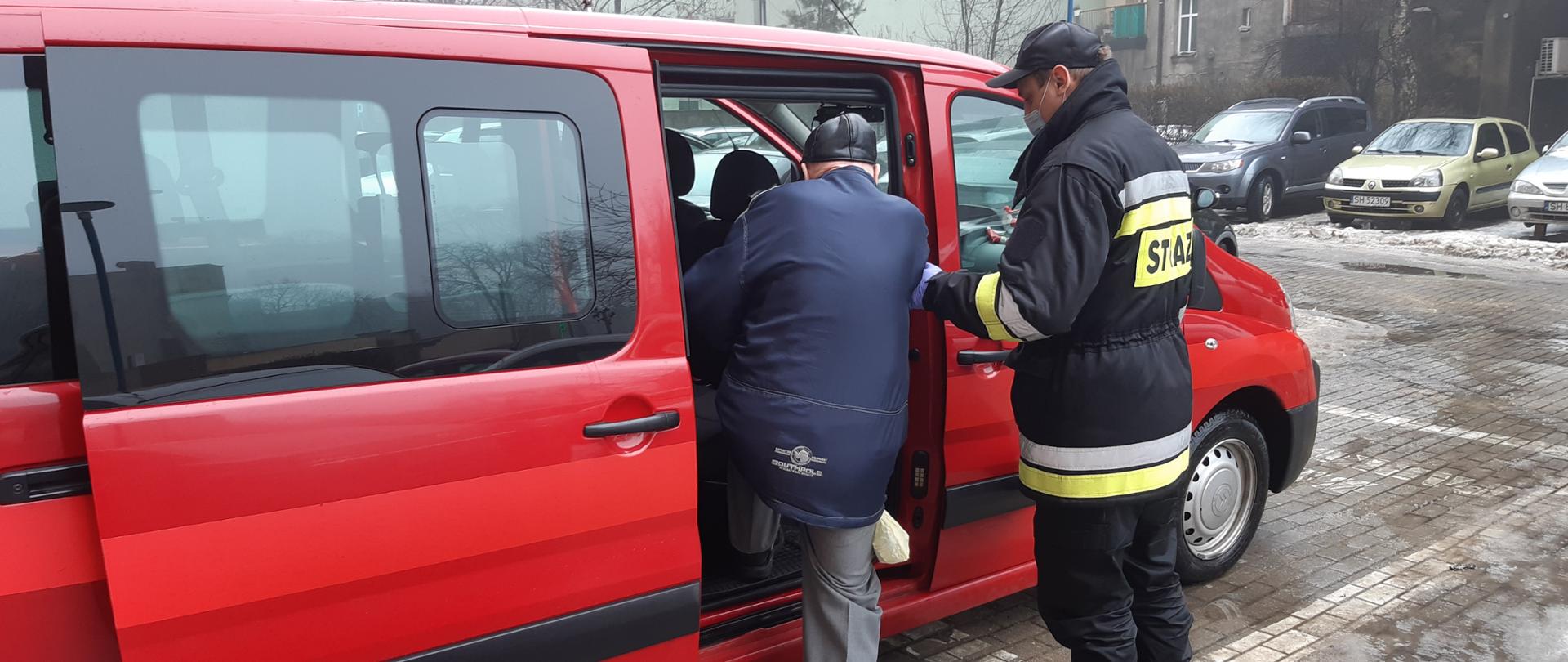 Zdjęcie przedstawia strażaka pomagającego wejść osobie starszej do samochodu pożarniczego typu BUS ze wzgledu na akcję szczepimy się.